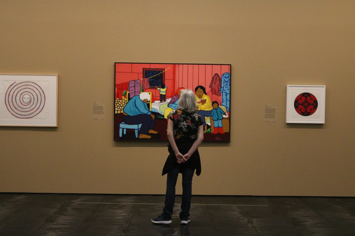 A visitor seen from behind before a large colourful painting on an ochre wall, flanked by two smaller works. Foto: Rovena Rosa/Agência Brasil