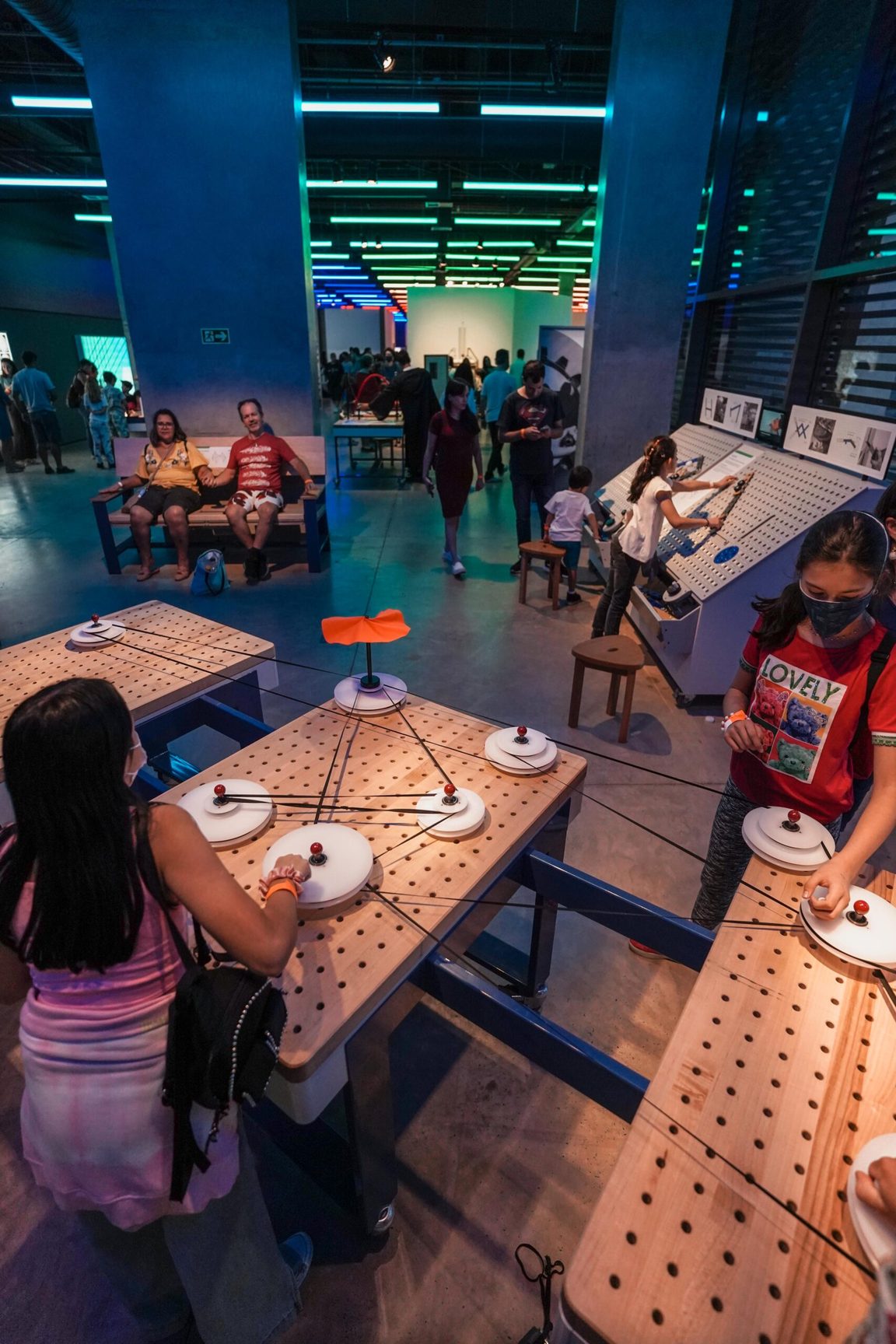 Visitors gathered around tables of hands-on exhibits in the blue hall of SESI Lab. Foto: Pelicano Filmes